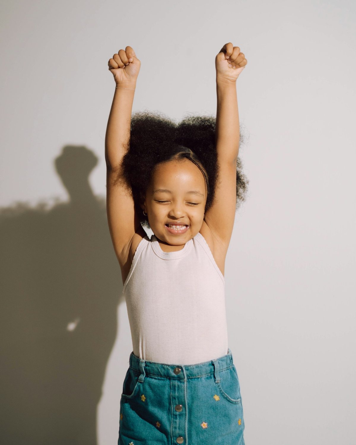 A young girl with both arms raised, eyes closed, celebrating