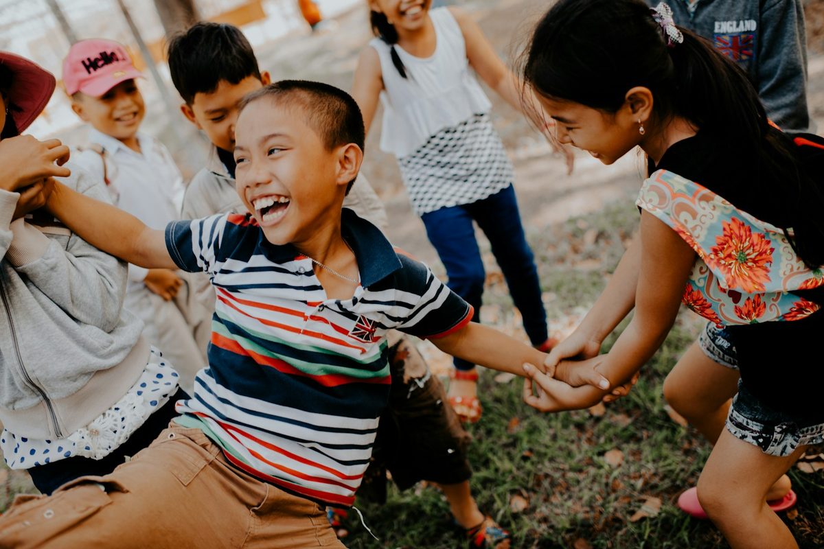 A group of children holding hands and laughing while playing outdoors